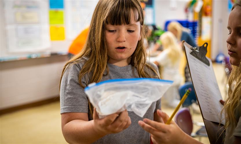 A girl with brown hair looks at an item in a plastic bag